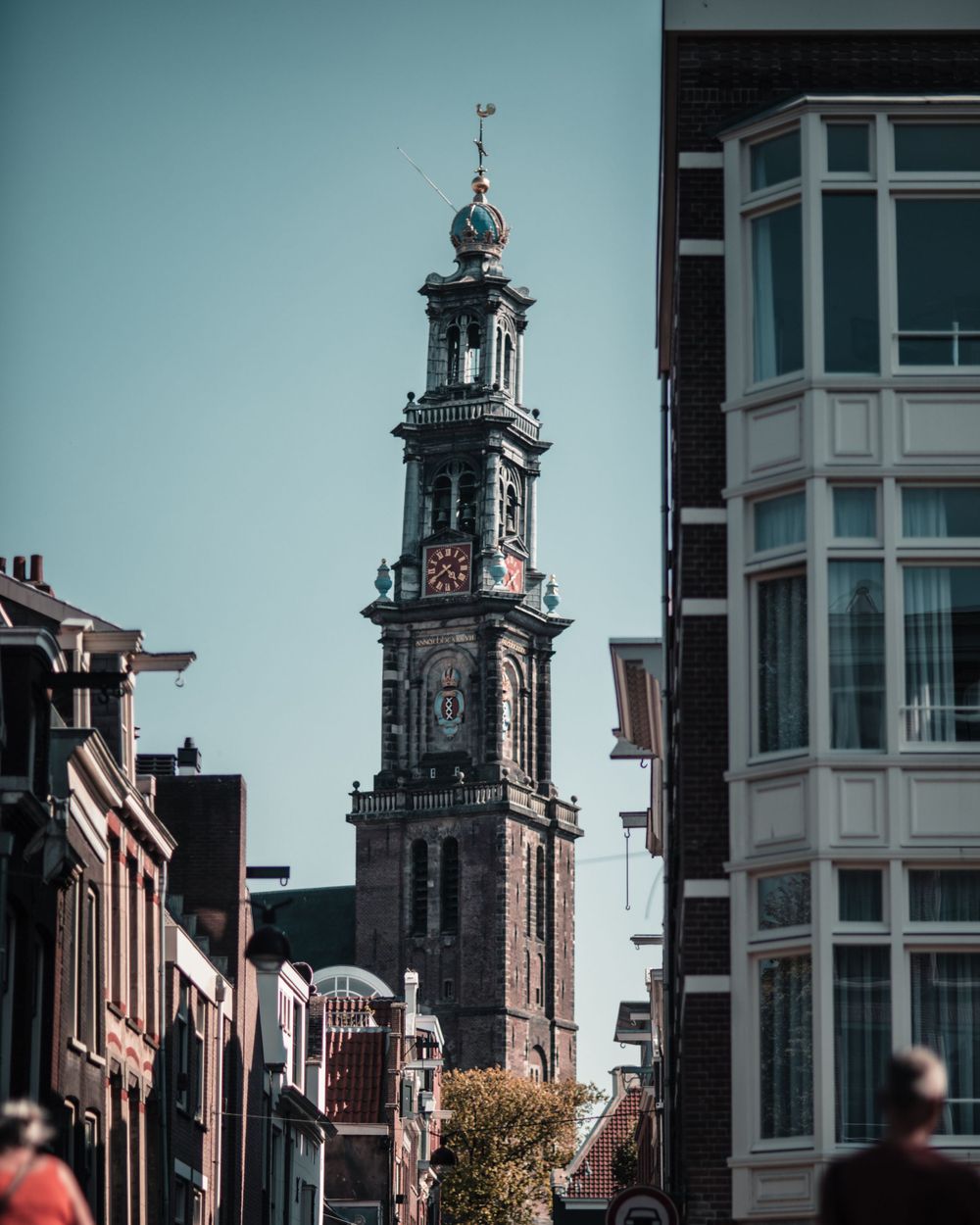 Historic church tower with ornate clock face rising above Amsterdam city buildings.