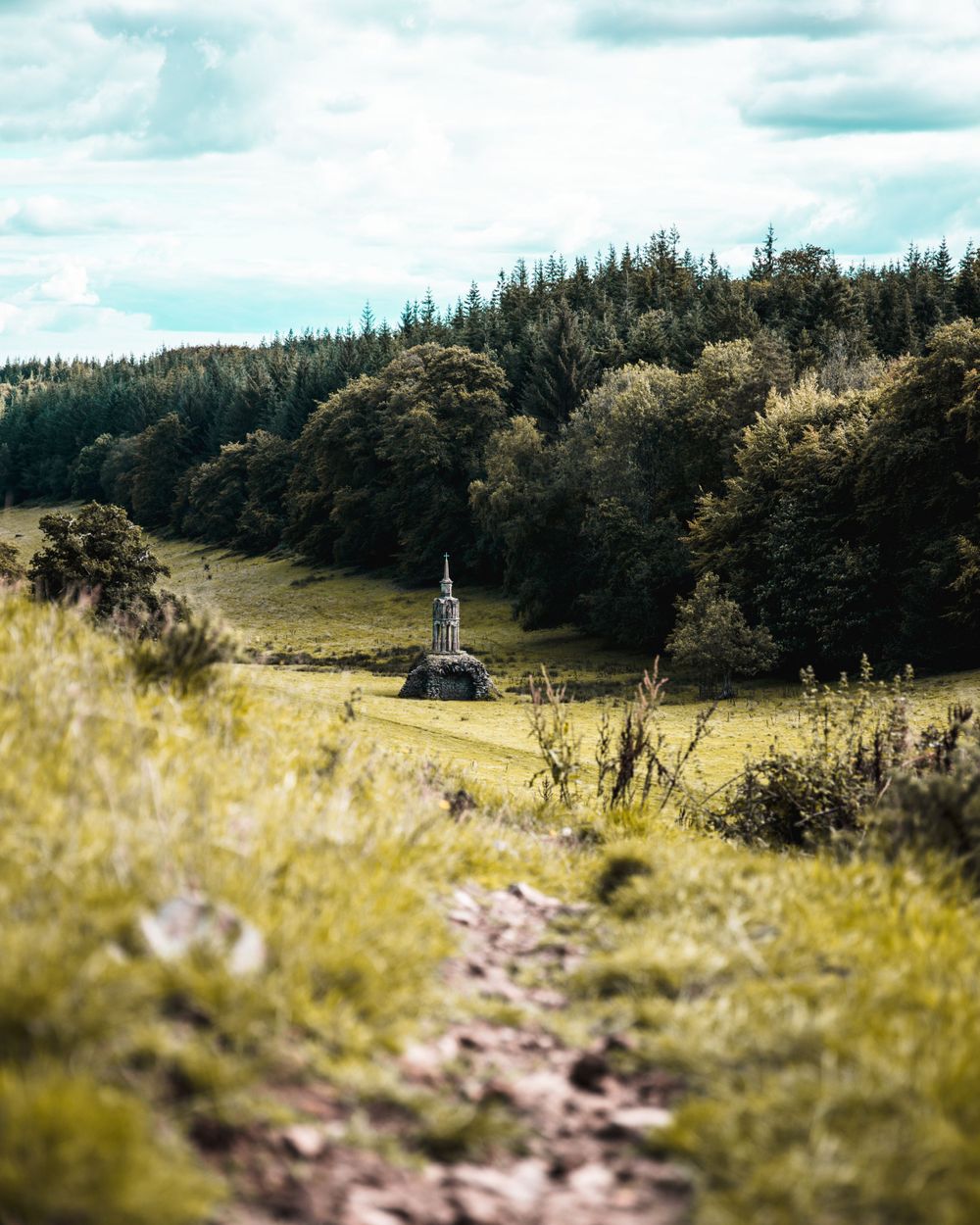 Small church steeple nestled in a pastoral landscape with forest-covered hills.