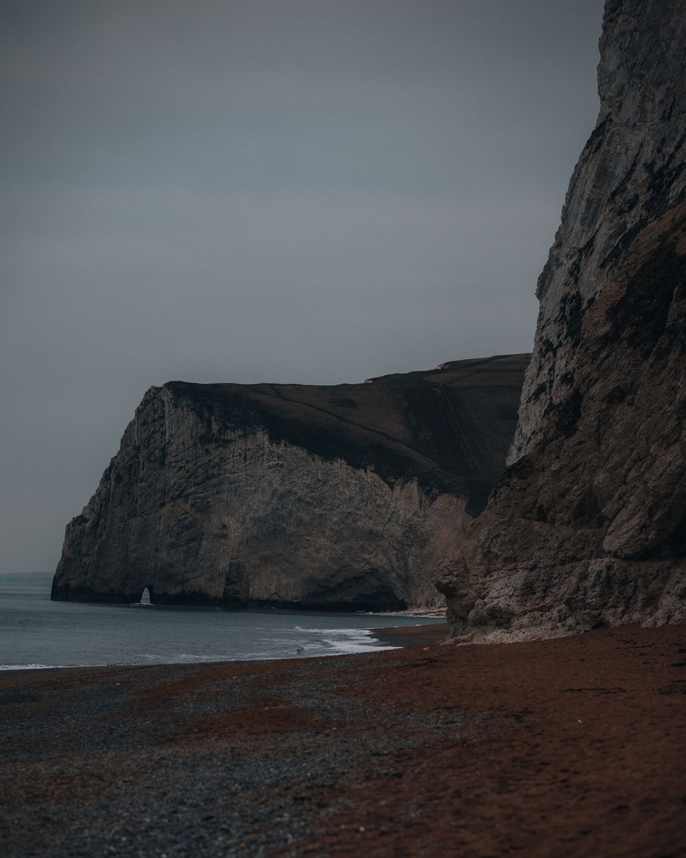 Dramatic coastal cliffs and beach landscape under moody gray skies.