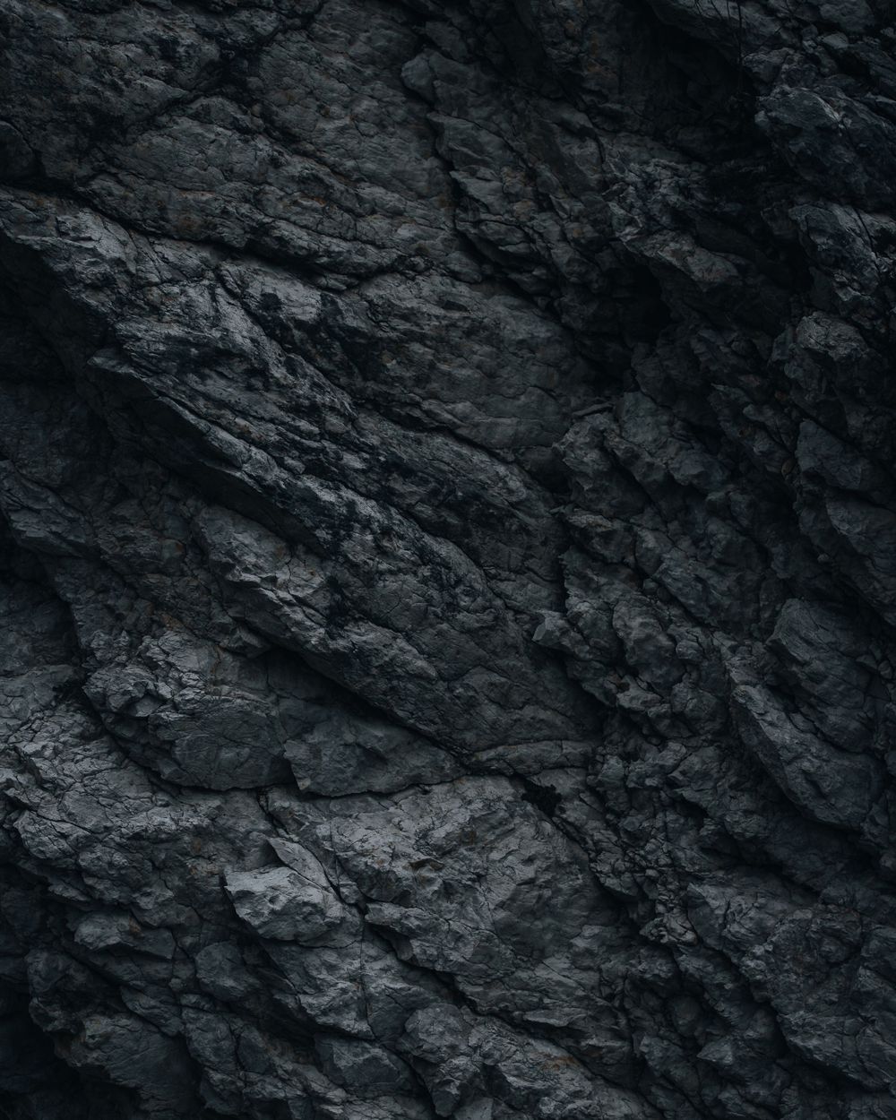 Close-up texture of dark rocky cliff face with jagged surfaces and natural patterns.