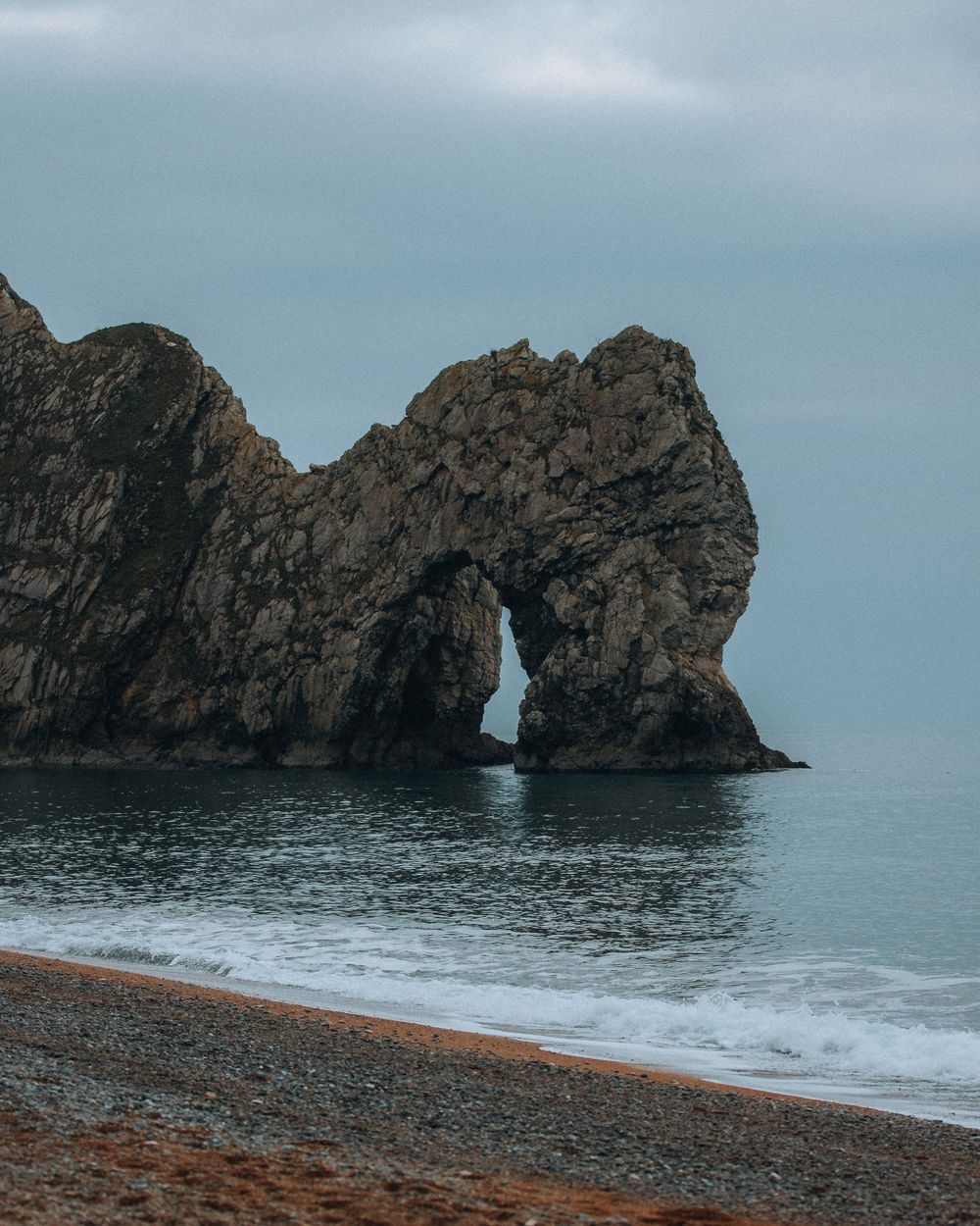 Durdle Door natural limestone arch formation rising from the sea against cloudy sky.