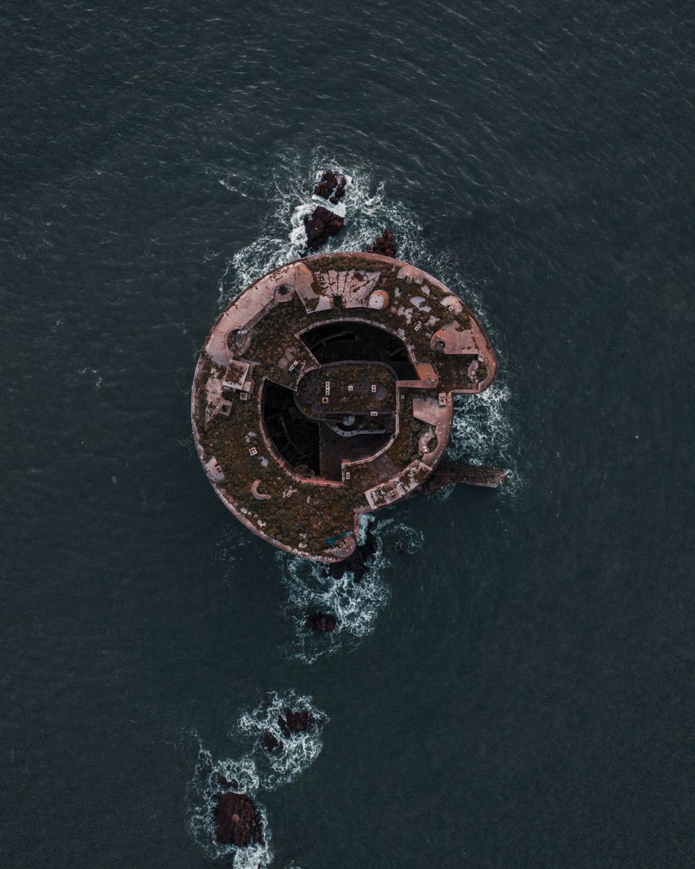 Aerial view of a rusty circular buoy floating in dark ocean waters.
