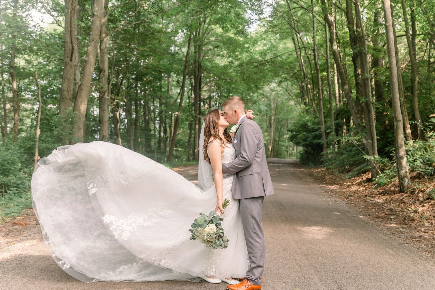 Couple takes romantic wedding photos on a tree-lined path with flowing white veil.