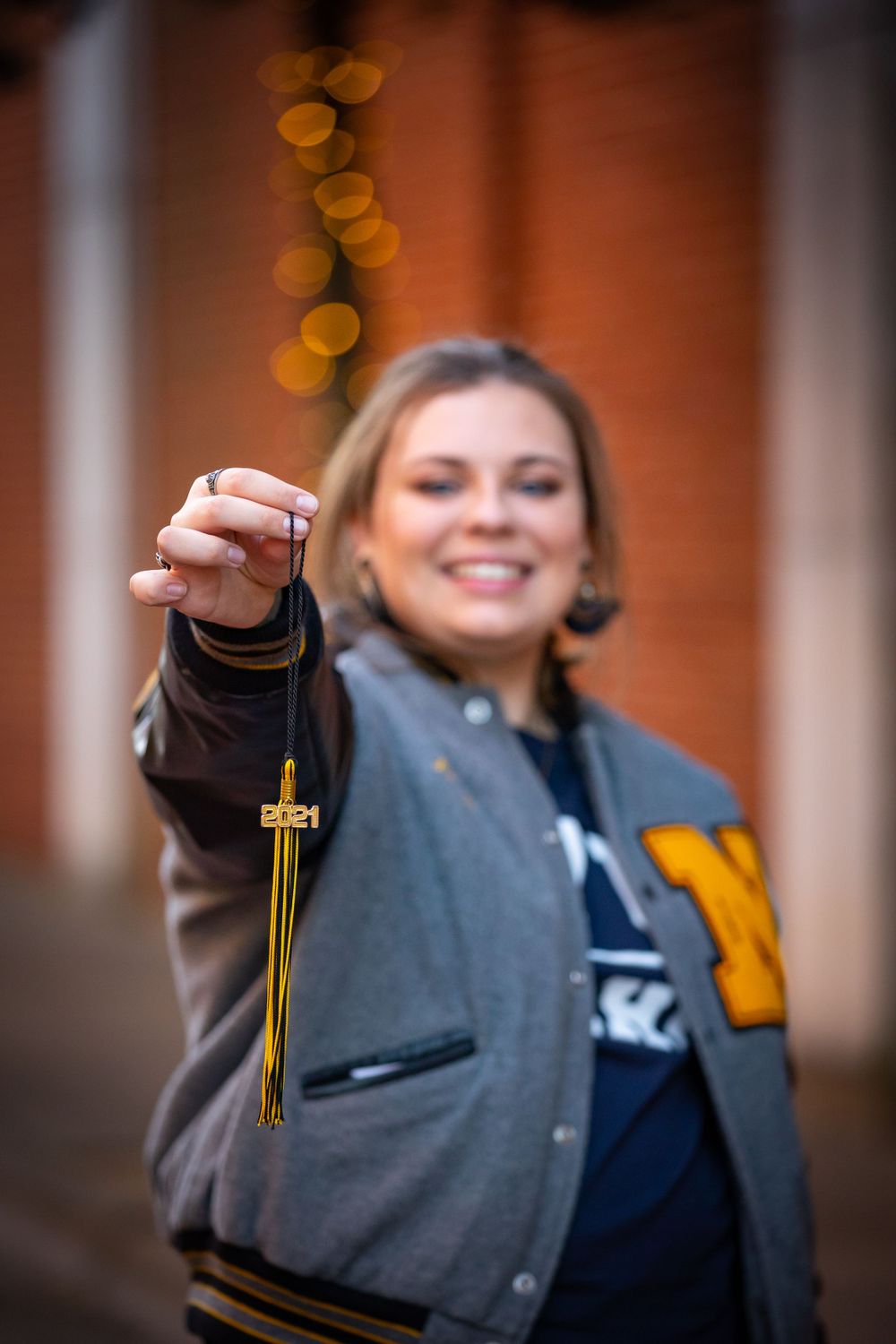 Graduate displaying tassel while wearing university letter jacket at dusk.