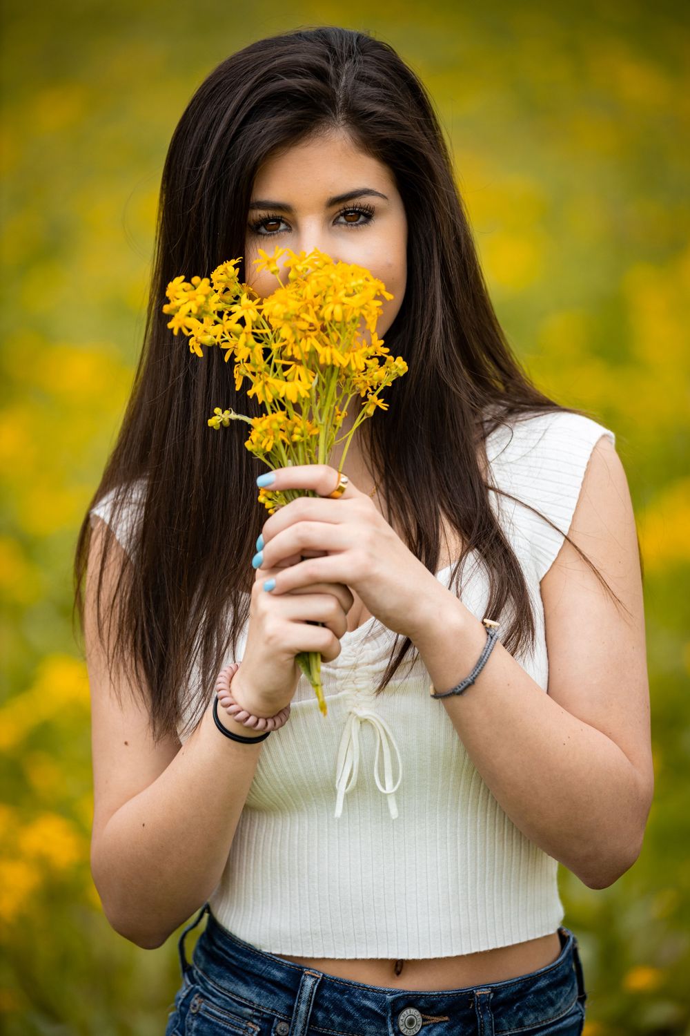 A person holds yellow wildflowers in a field, creating a cheerful summer portrait.