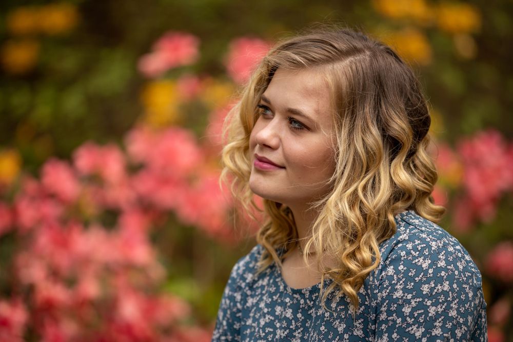 A dreamy portrait against pink flowers and autumn foliage creates a romantic garden scene.