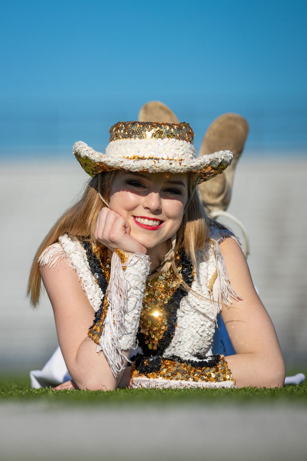 A western-themed portrait on grass featuring a decorative cowboy hat and white performance outfit.
