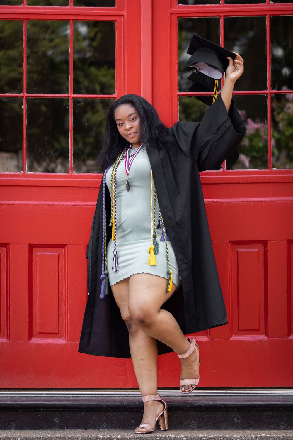 Graduate celebrating in black cap and gown against a bright red phone booth backdrop.