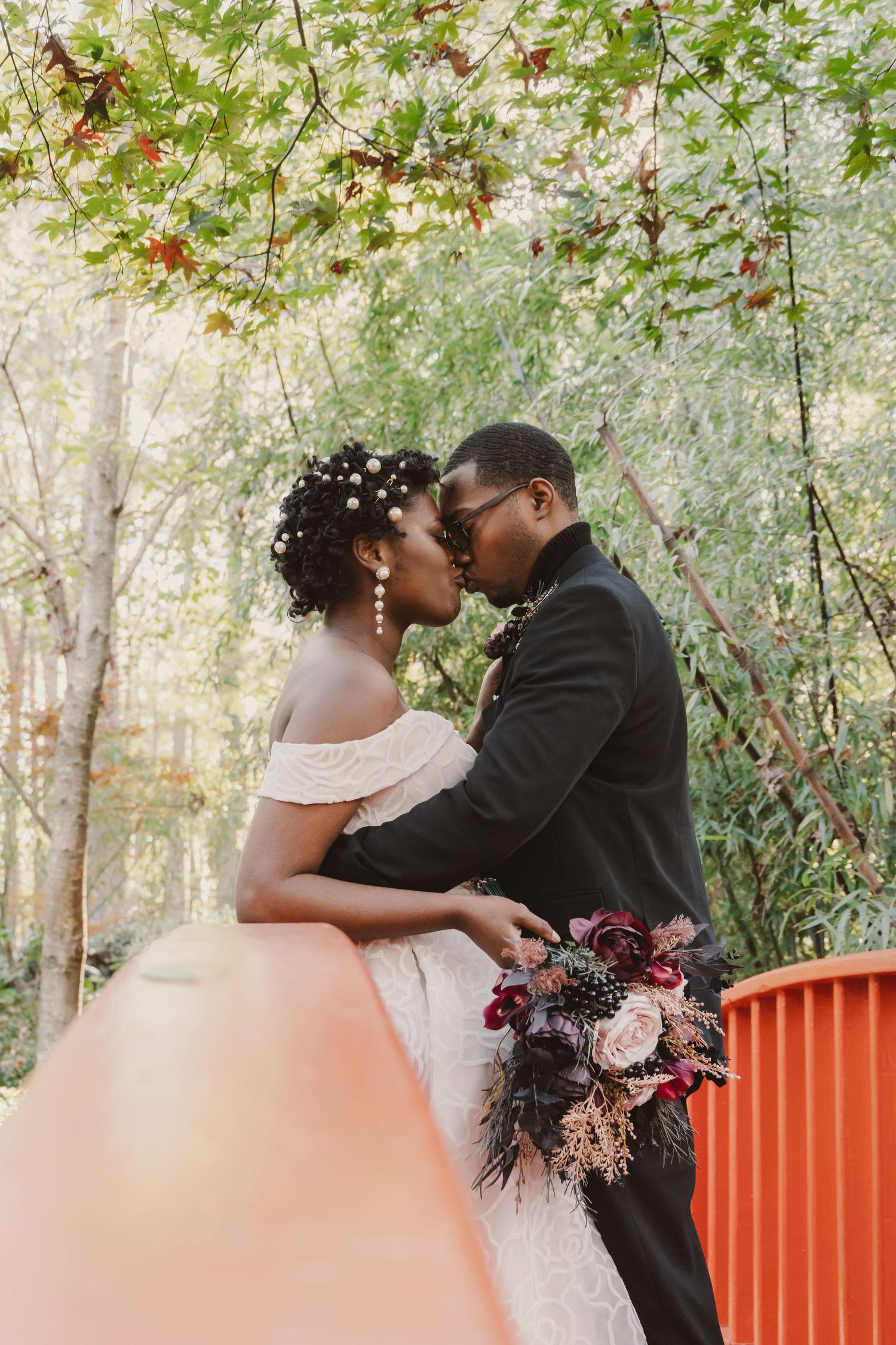 A newlywed couple kiss in an intimate elopement on a bridge, surrounded by nature.