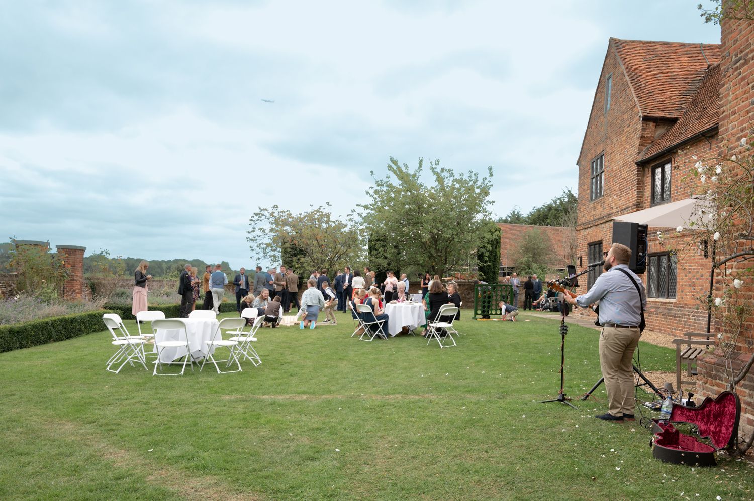 Casual outdoor wedding reception with guests seated on lawn and musician performing.