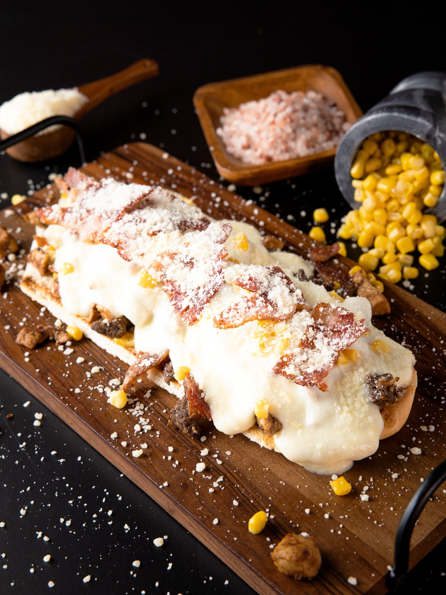 White burrito topped with melted cheese, corn and seasoning on rustic wooden board.