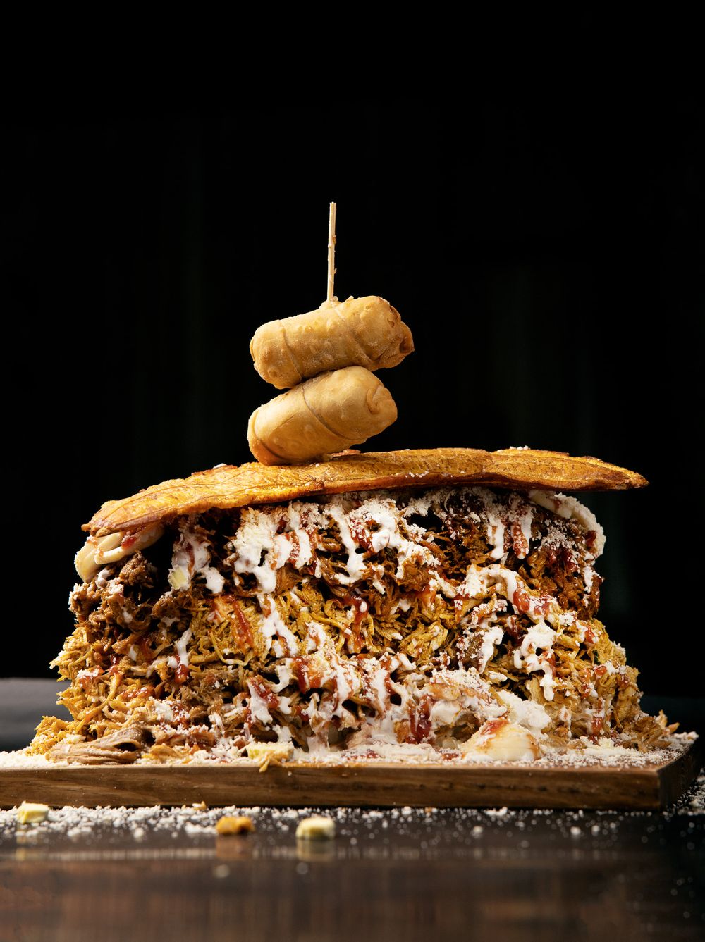 Multi-layered gourmet sandwich topped with onion rings showcasing intricate layers of meat and cheese.