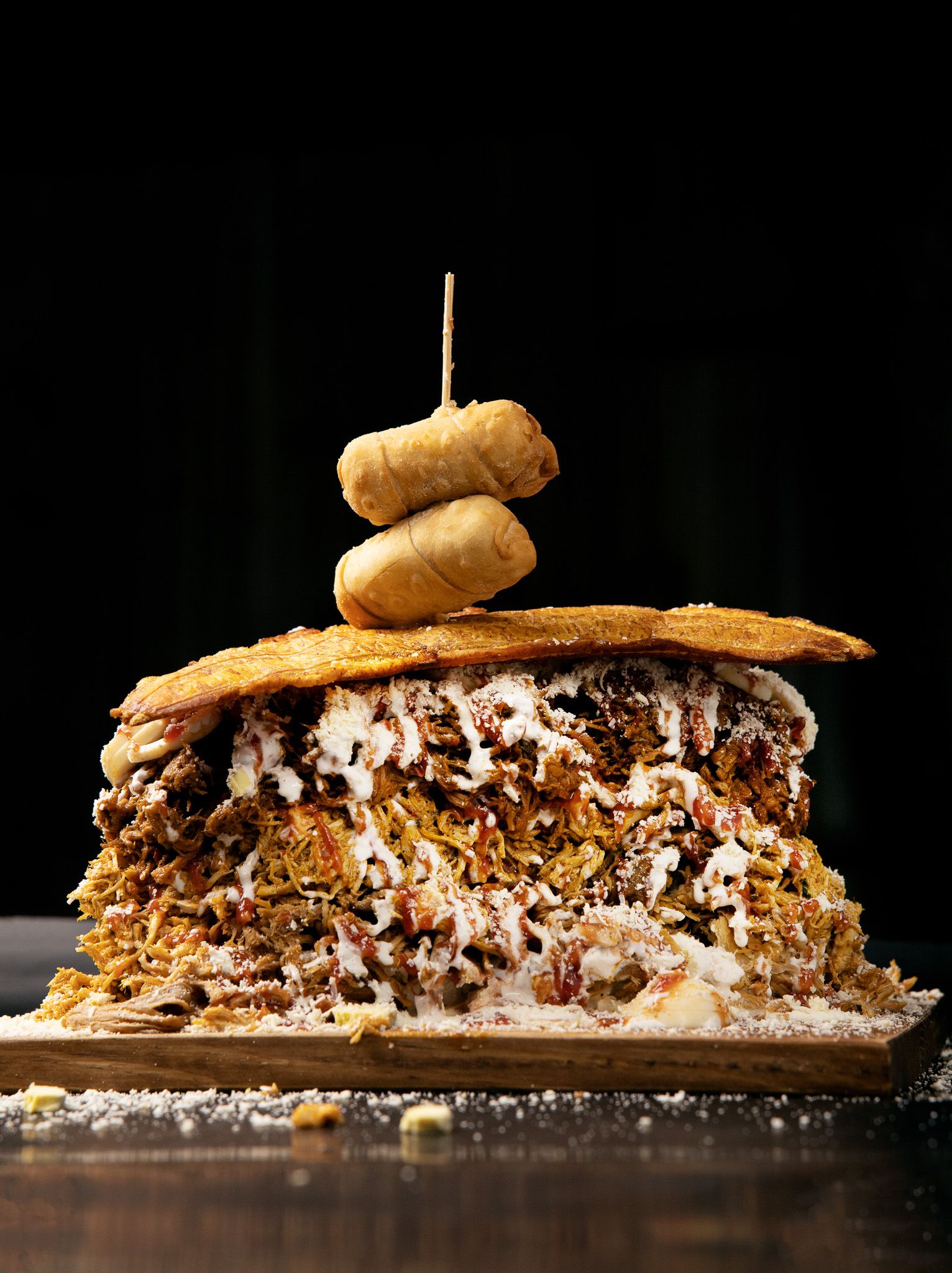 Multi-layered gourmet sandwich topped with onion rings showcasing intricate layers of meat and cheese.
