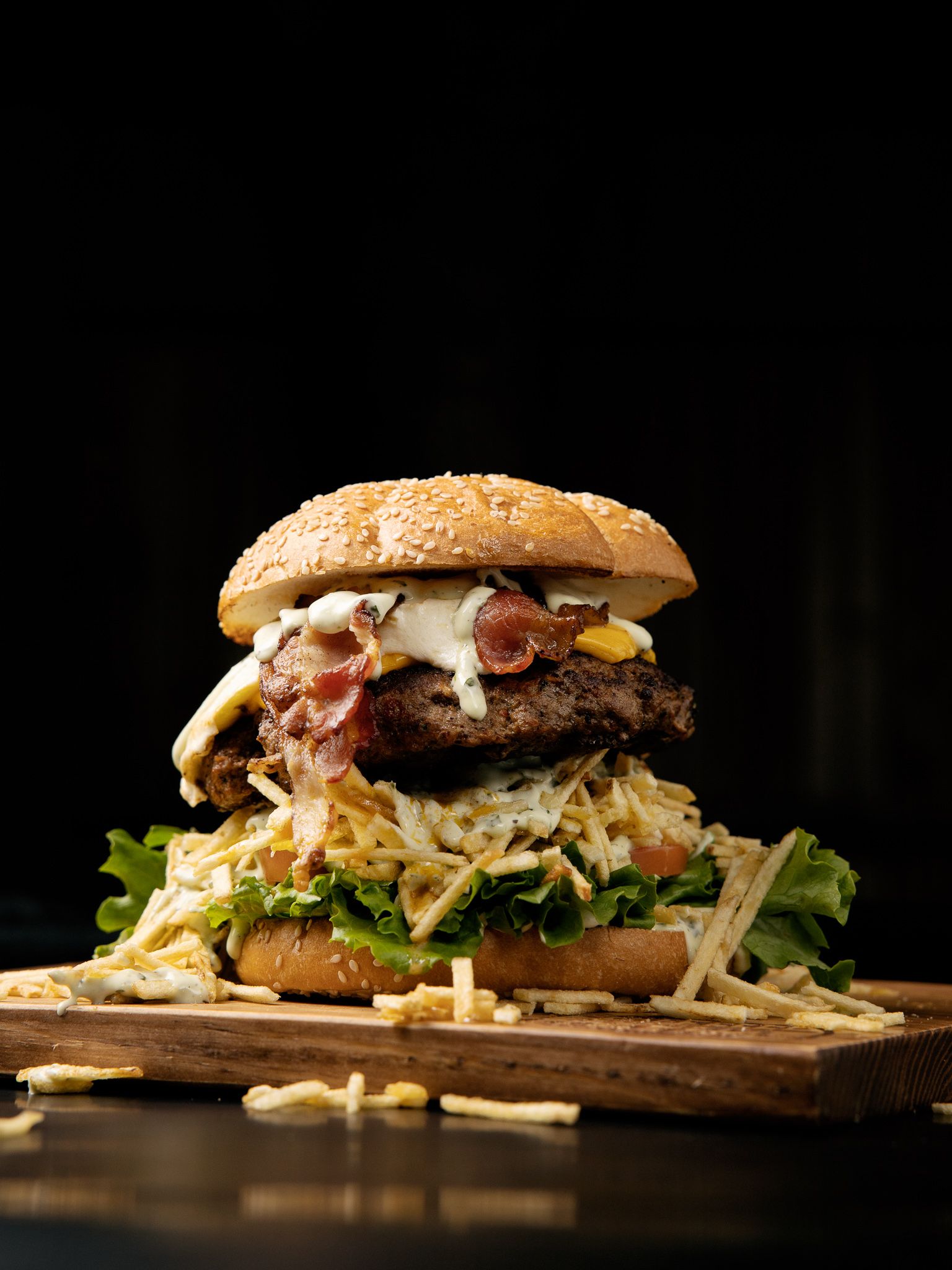Gourmet burger with bacon and coleslaw served on a wooden board against dark background.