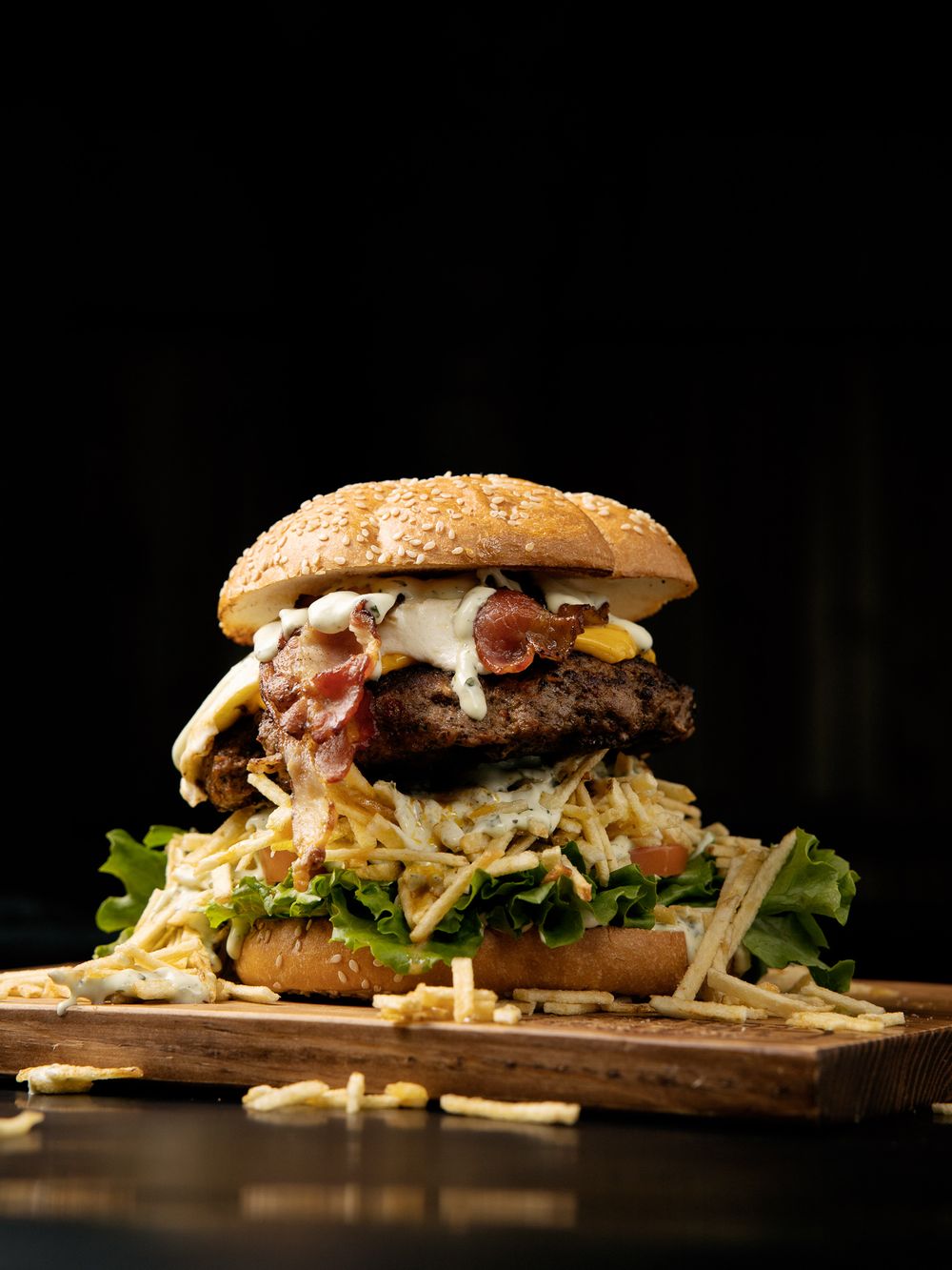 Gourmet burger with bacon and coleslaw served on a wooden board against dark background.