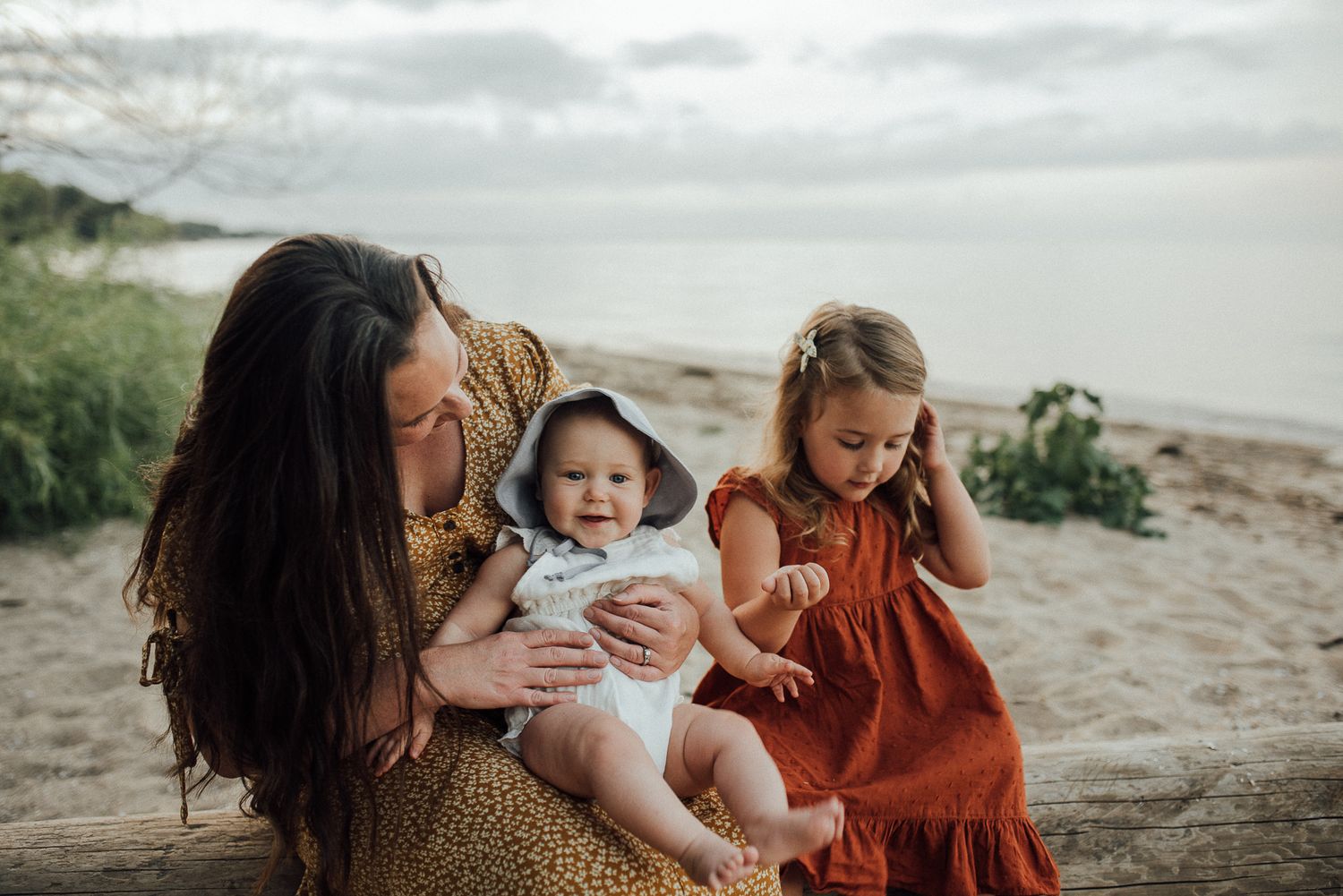 A heartwarming family moment on a beach with a mother and children in mustard yellow and rust-colored dresses.