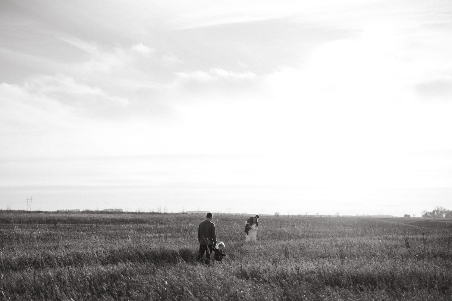 Black and white landscape photo of two figures walking through a vast grassy field.
