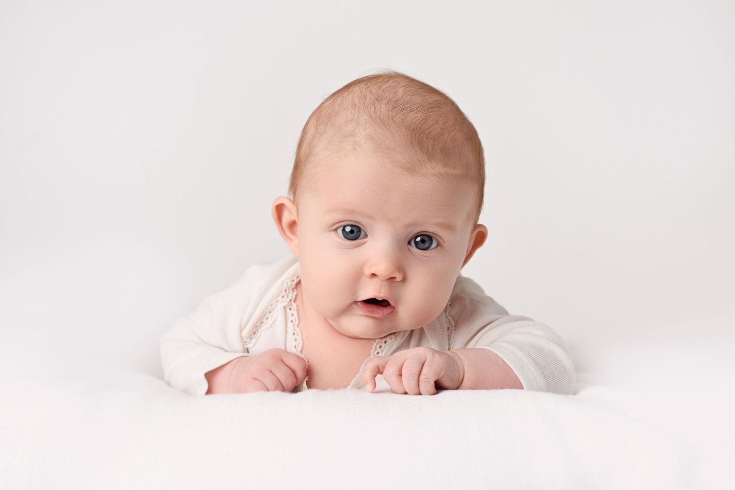 A baby lying on their stomach during a minimalist white studio portrait session.
