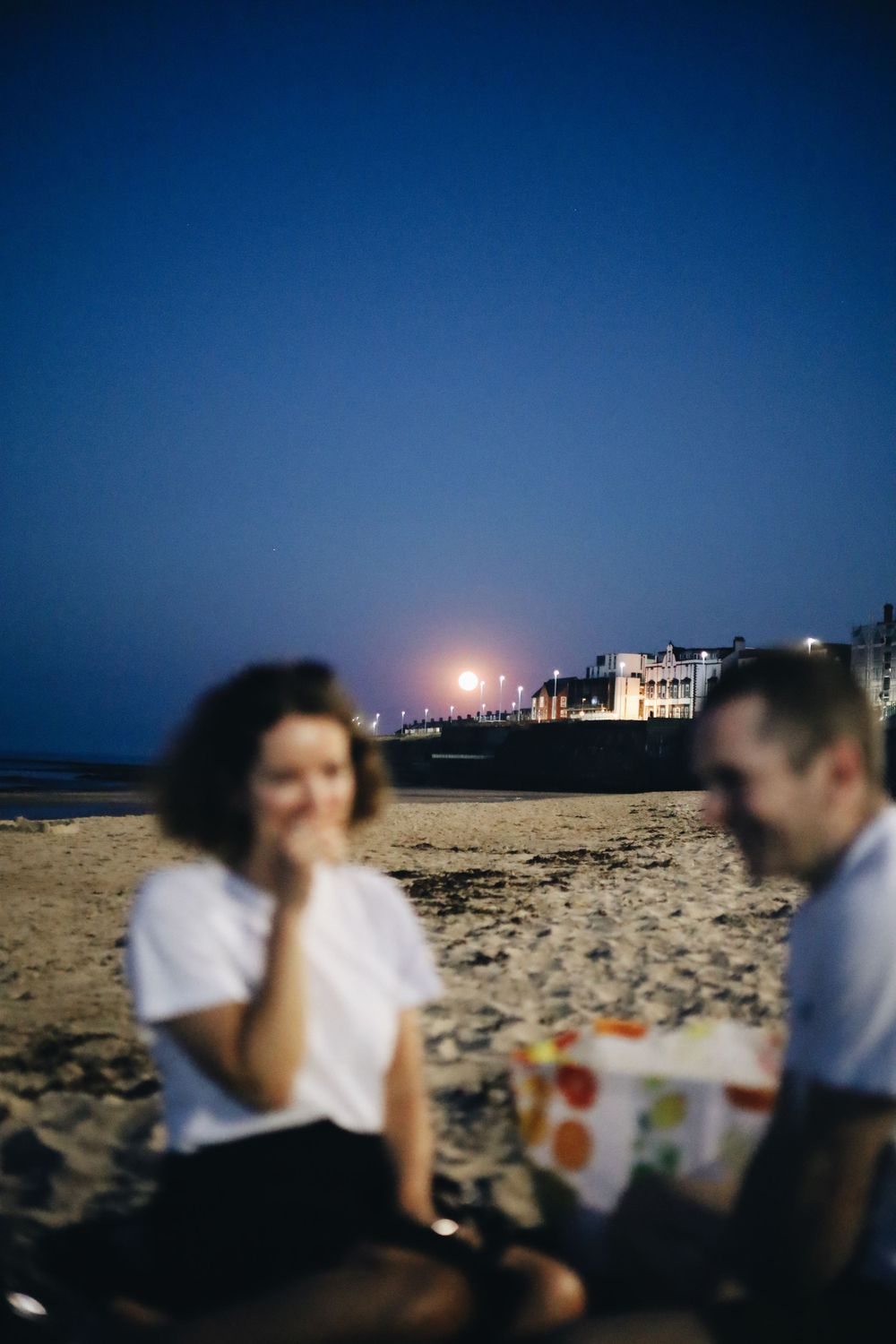 Night scene at a beach with city lights glowing in the distance.