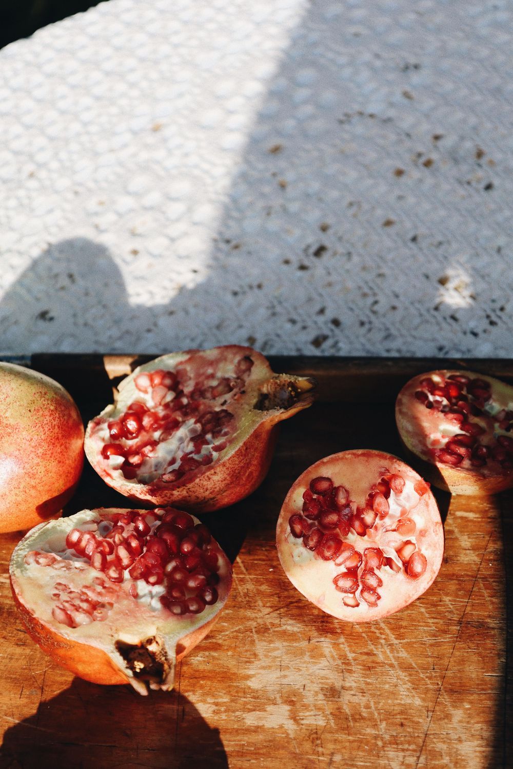 Fresh pomegranates split open on a wooden cutting board revealing bright red seeds inside.