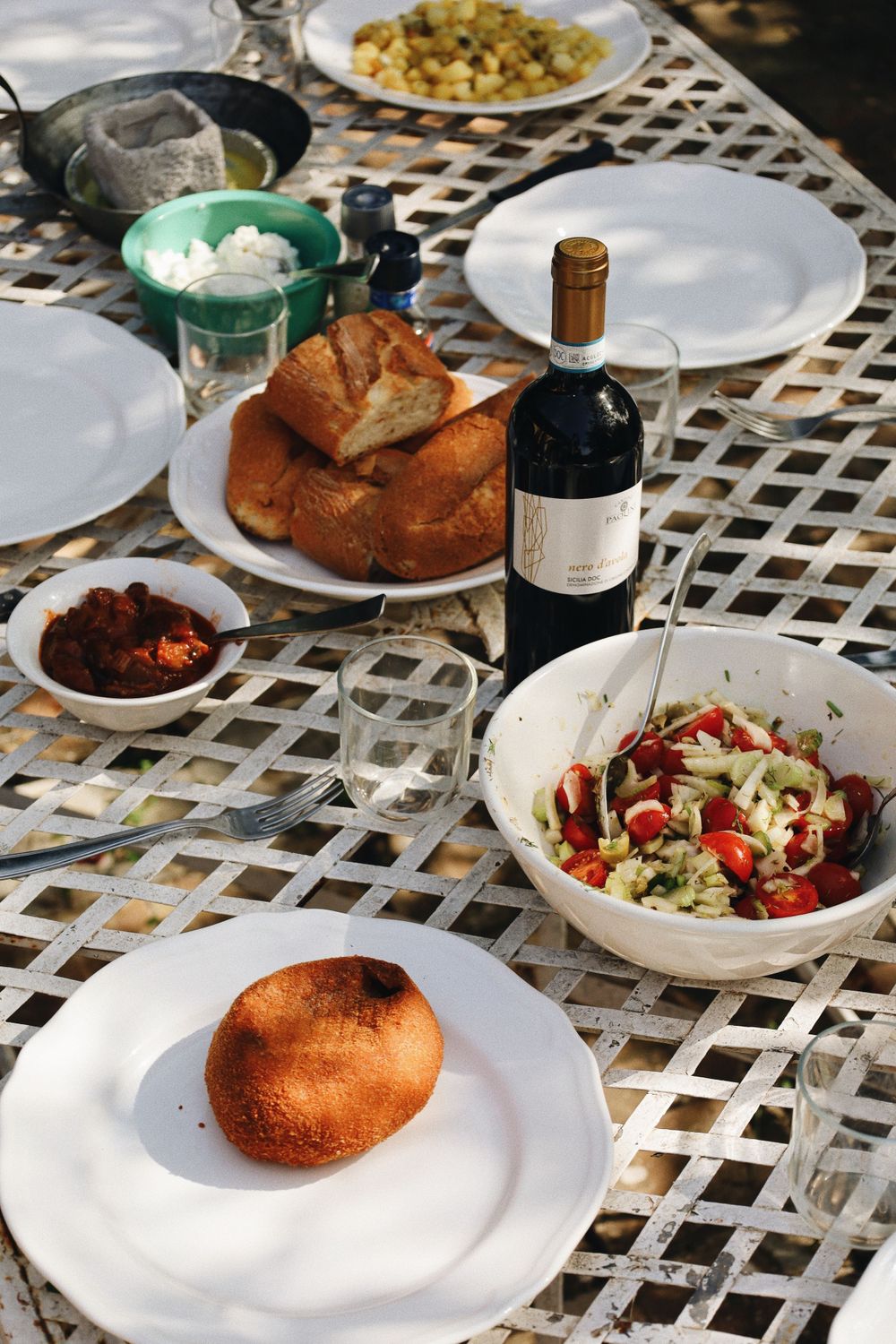 An outdoor dining table set with white plates and fresh salads on a latticed surface.