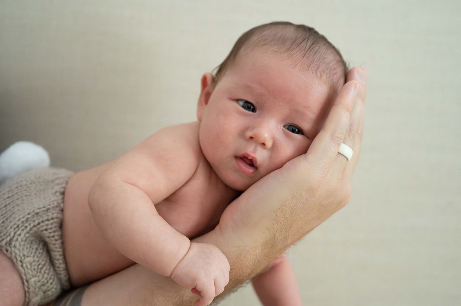 A newborn baby rests peacefully against a caregiver's hand.