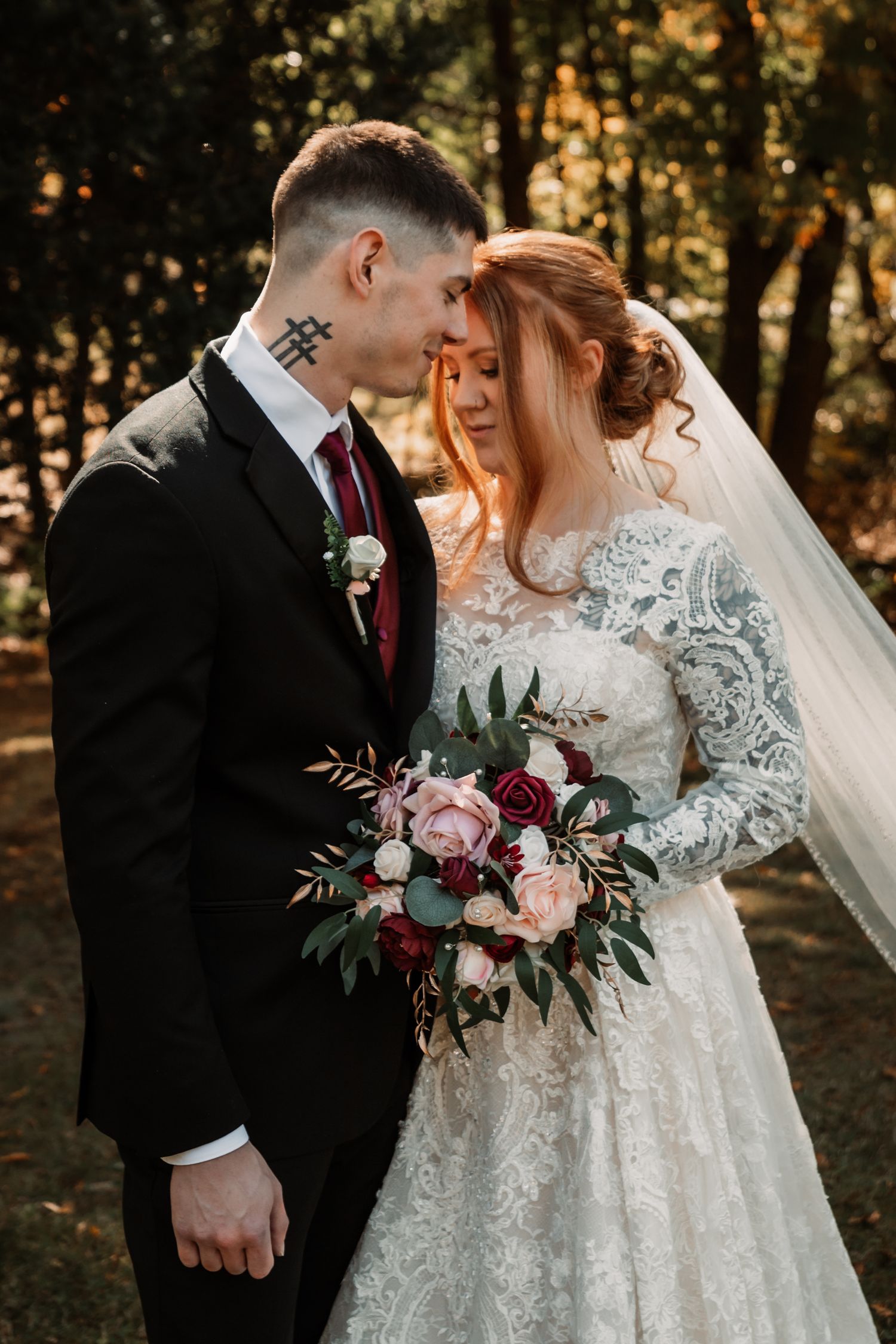 A romantic wedding portrait with red and pink florals in a wooded setting.