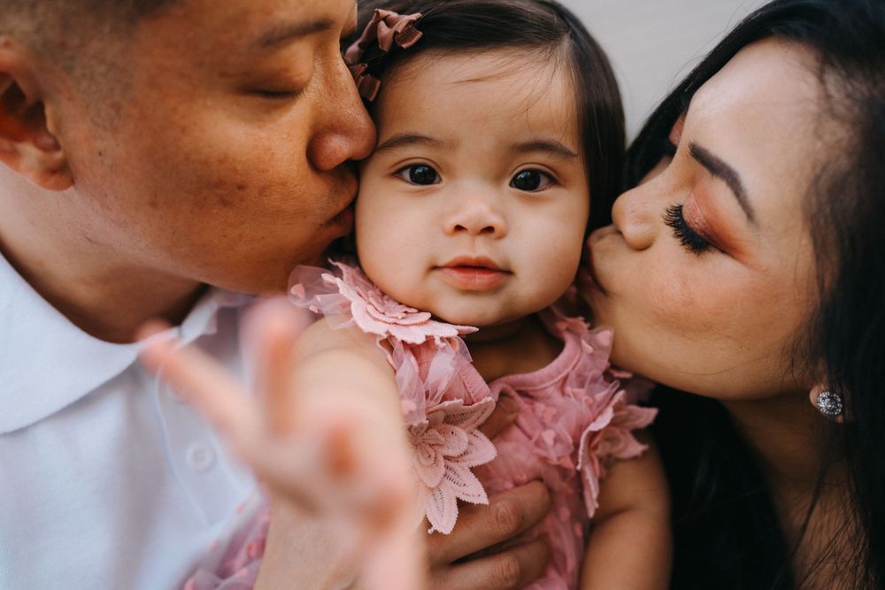 Family members share tender kisses with a baby wearing a pink dress in a series of connected photos.