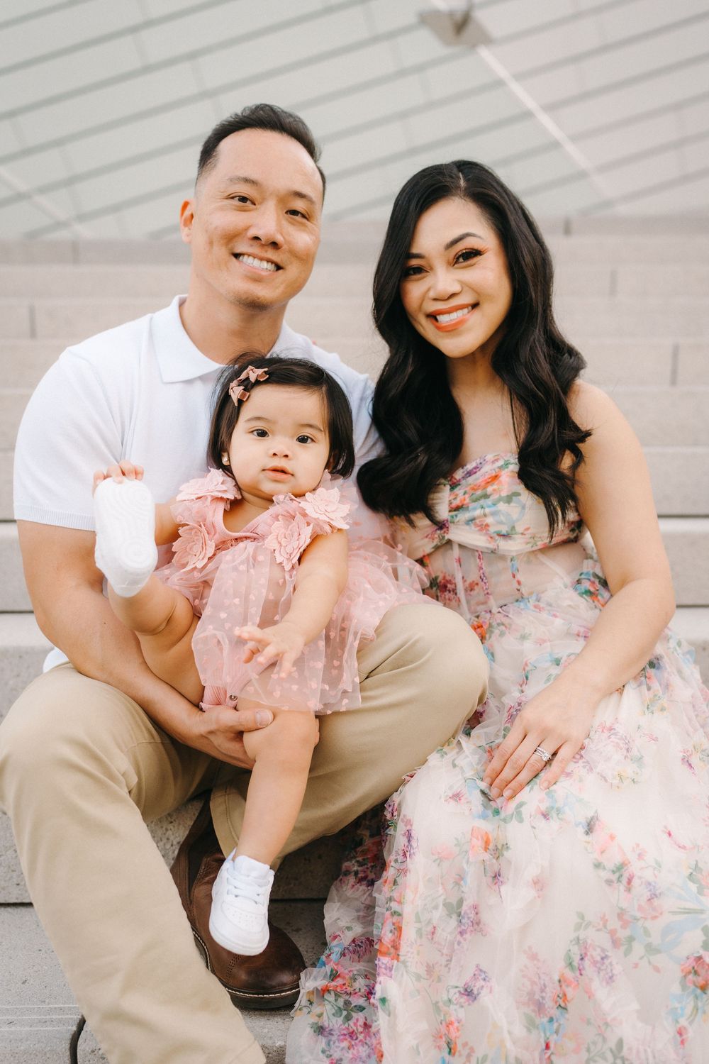 Family wearing coordinated pink and beige outfits poses together in a bright indoor setting for professional photos.