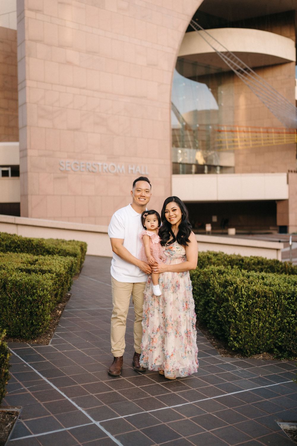 A family shares tender moments together outside a modern building with stone walls and manicured hedges.
