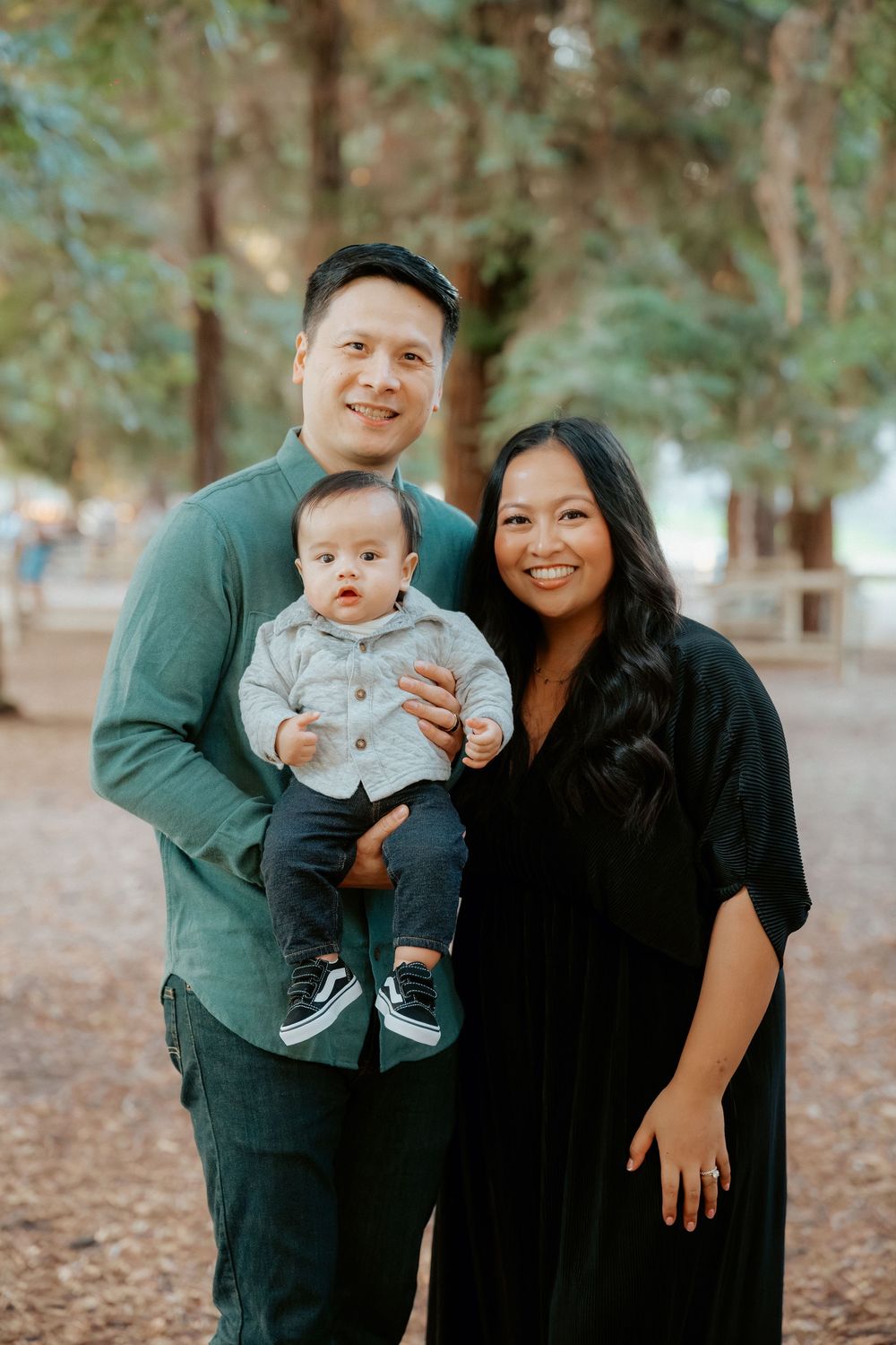 A family poses together in a wooded outdoor setting wearing coordinated dark clothing.