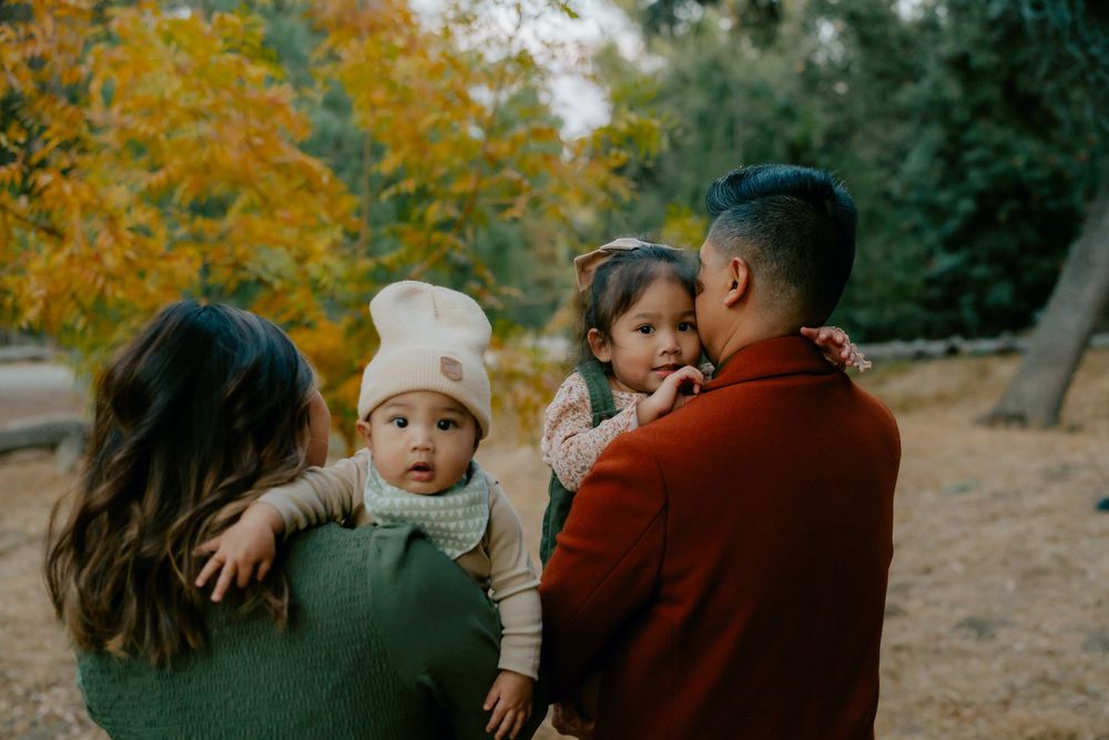 A family shares tender moments together in an autumn setting with golden foliage in the background.