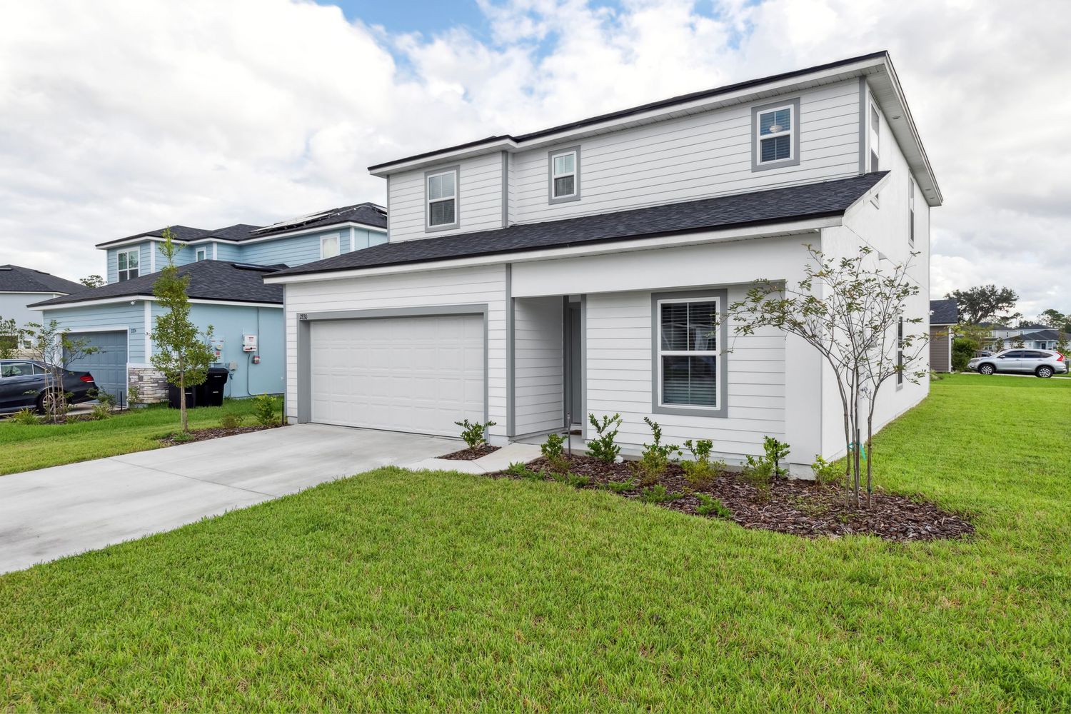 Modern two-story white home with gray accents featuring attached garage, manicured lawn and fresh landscaping.