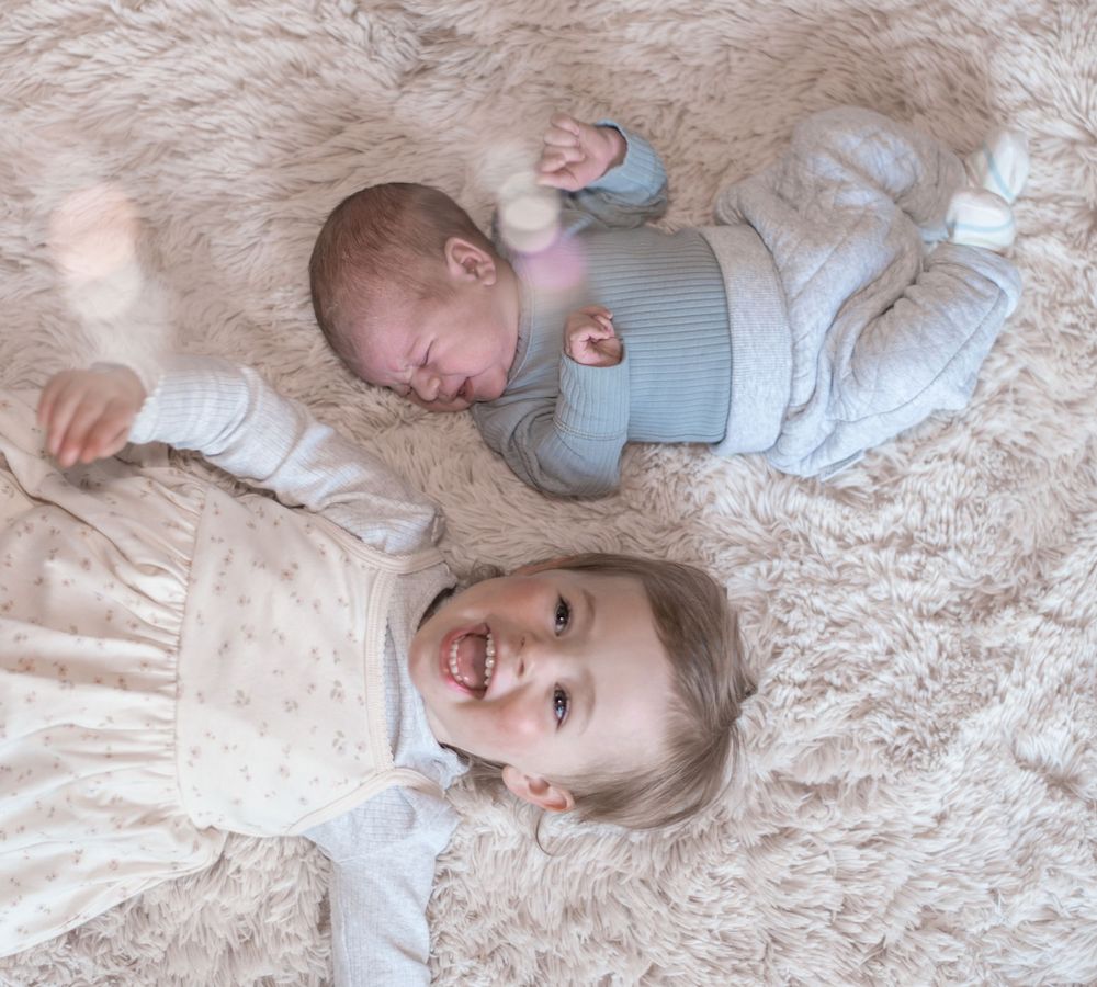 A sequence of photos showing a baby in a gray onesie playing and laughing while lying on a plush beige carpet.