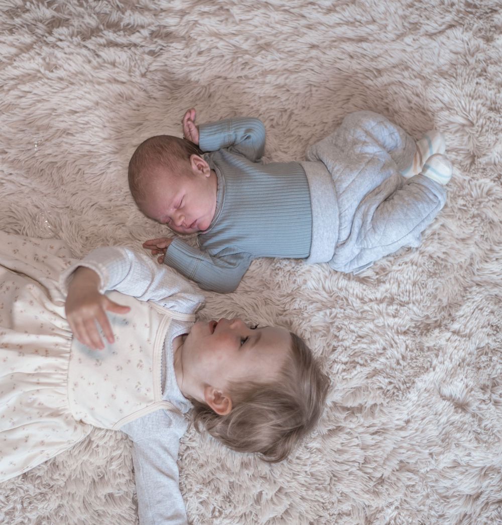 A baby wearing a gray sweater lies peacefully on a soft beige carpet in various resting positions.
