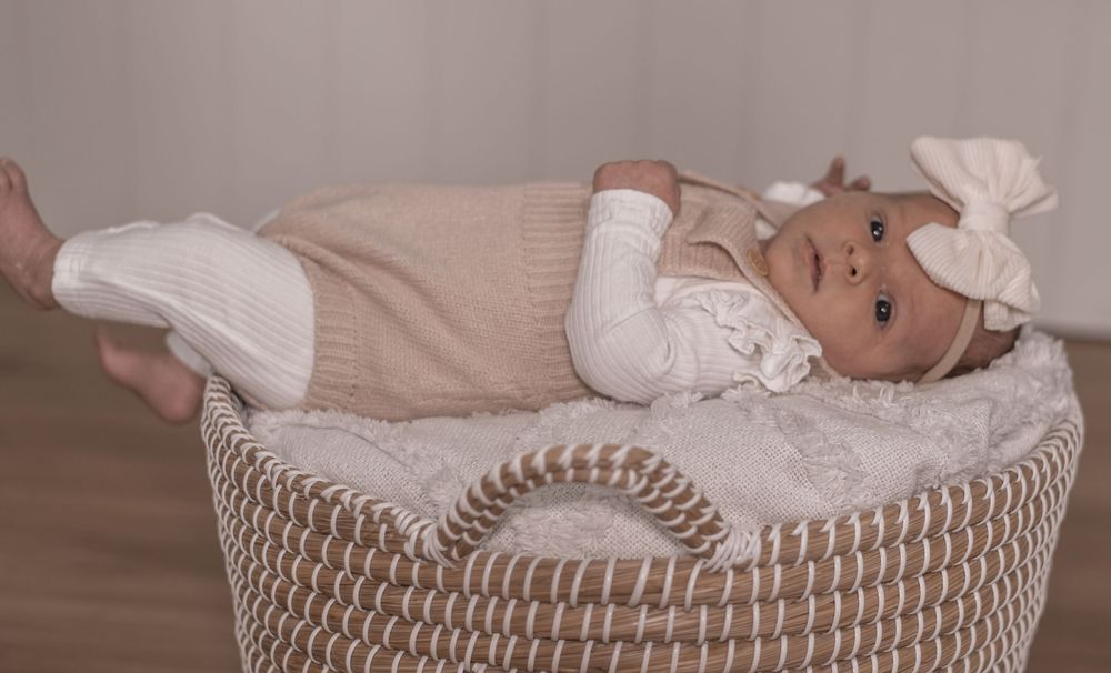 Baby resting peacefully in woven basket with white blanket and neutral tones.