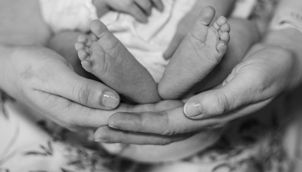 Black and white close-up images of tiny baby feet and hands being gently held.