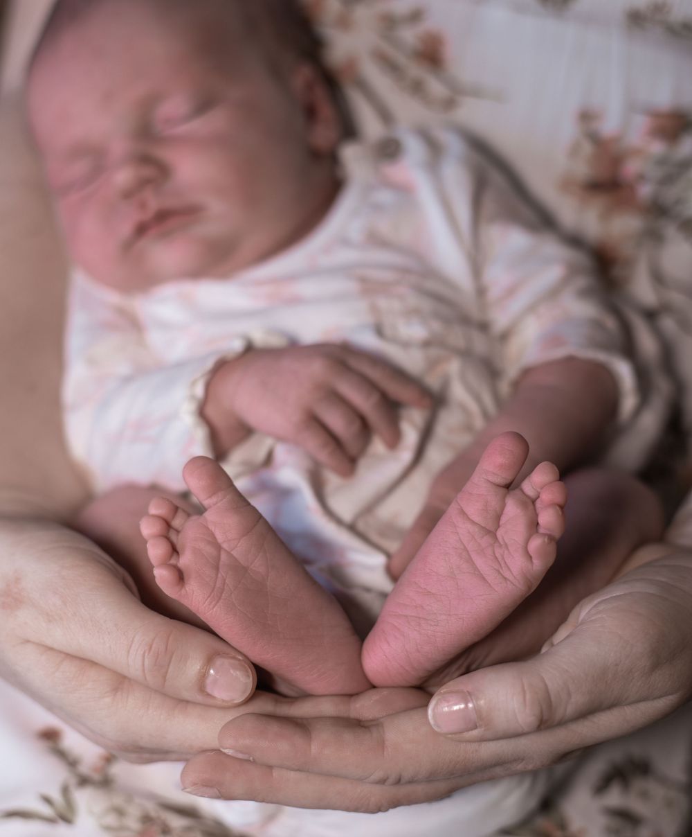 Tiny baby feet rest gently in caring hands while sleeping peacefully on a floral patterned blanket.