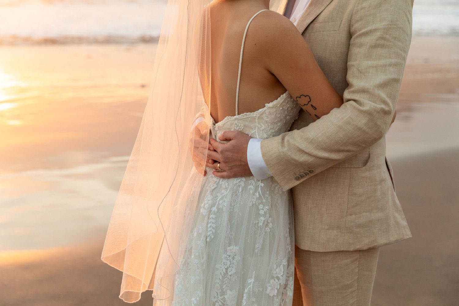 A romantic moment captured on a beach at sunset, as the bride and groom lovingly embrace each other.