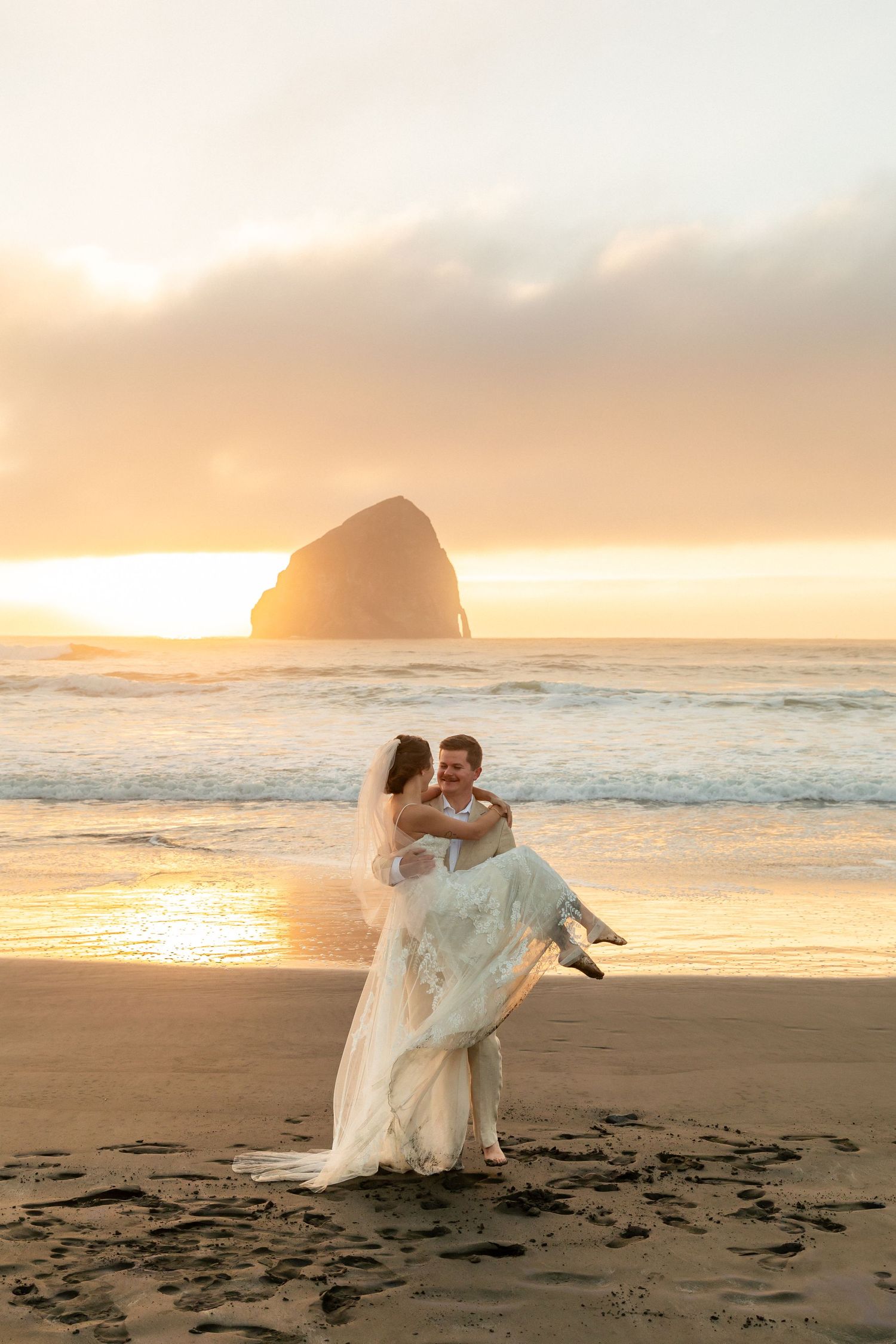 A romantic couple, dressed in wedding attire, standing on a sandy beach at sunset, with the ocean waves gently crashing
