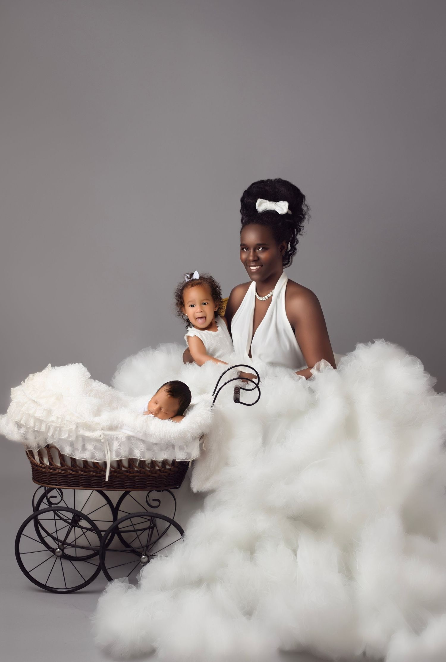 Studio portrait with antique pram and flowing white dress against grey backdrop.