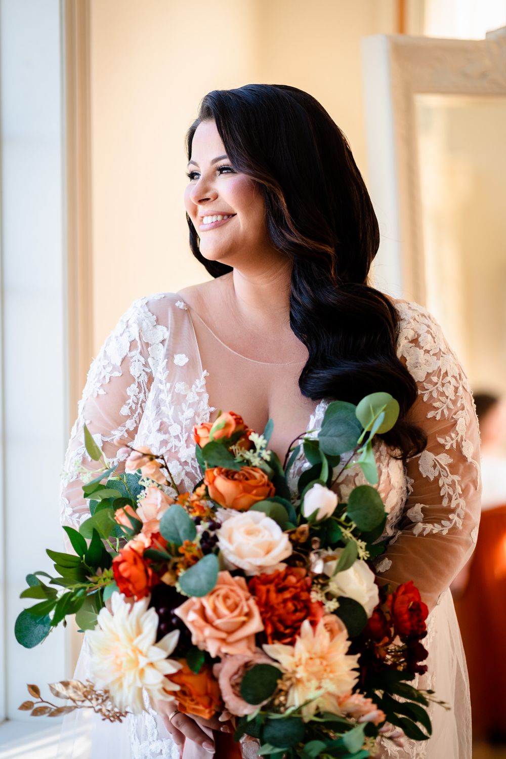 Bride holds stunning autumn-colored bouquet with orange and peach flowers.