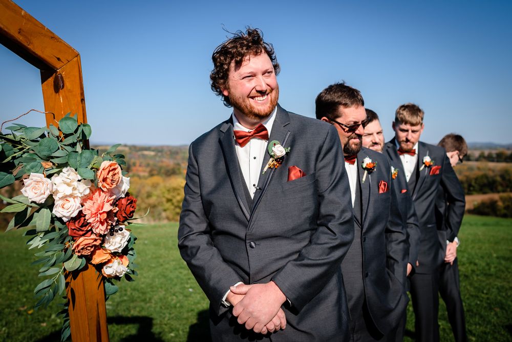 Wedding party celebrating outdoors with wooden arch and floral decorations against blue sky.