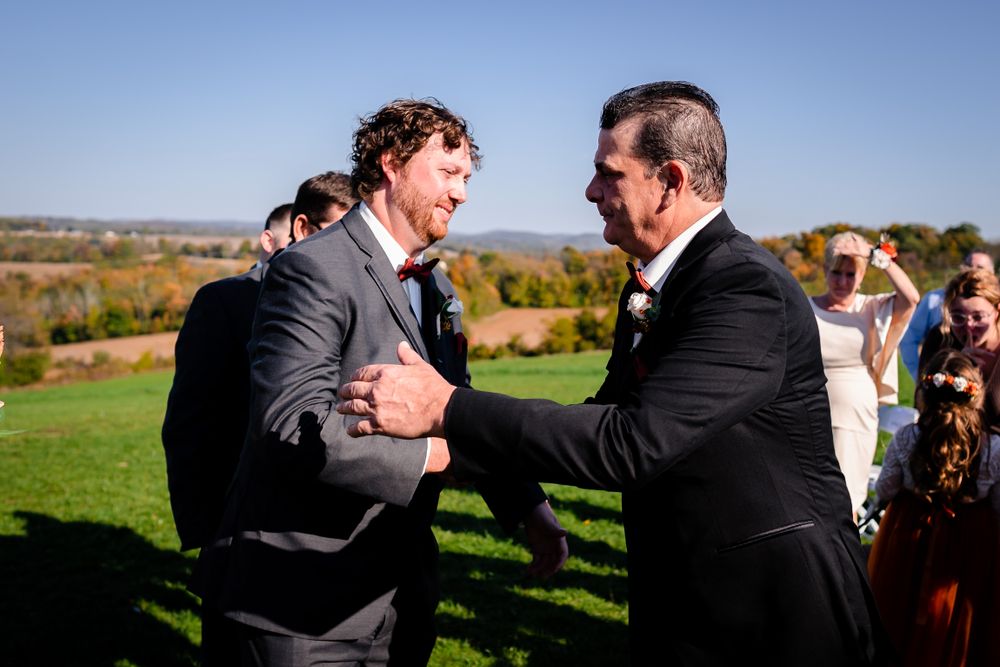 Groomsmen share heartfelt hugs outdoors against blue sky.