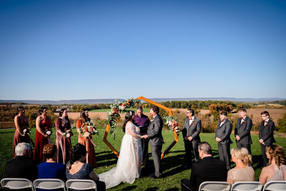 Wedding ceremony guests gathered on grassy hilltop with panoramic mountain views.