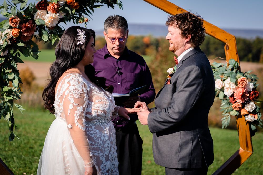 Wedding ceremony under wooden arch decorated with orange and pink flowers in outdoor setting.