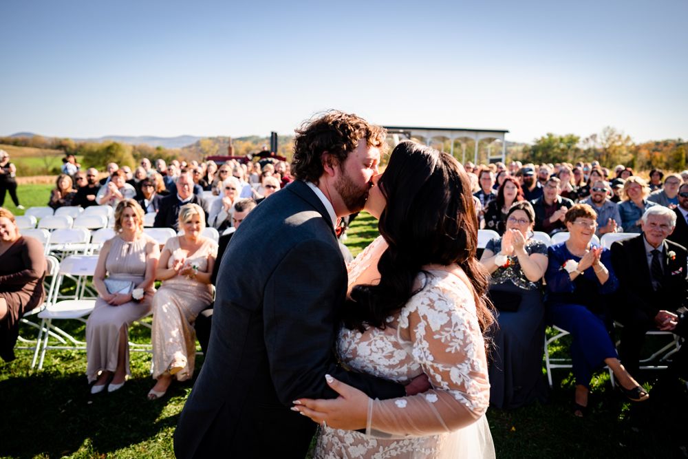 Large crowd of wedding guests watching ceremony on sunny autumn day outdoors.