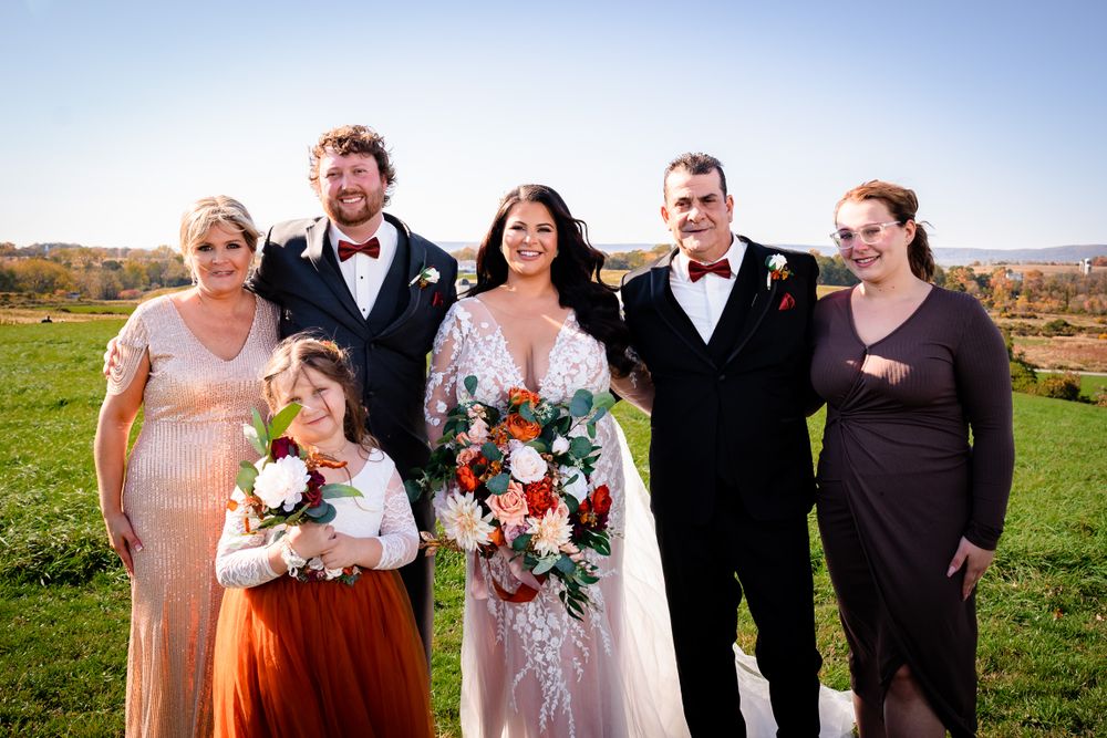 Wedding party members in formal attire posing together on grassy hillside.