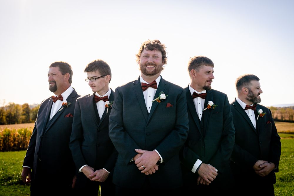 Groomsmen in black suits standing in line during outdoor wedding ceremony.