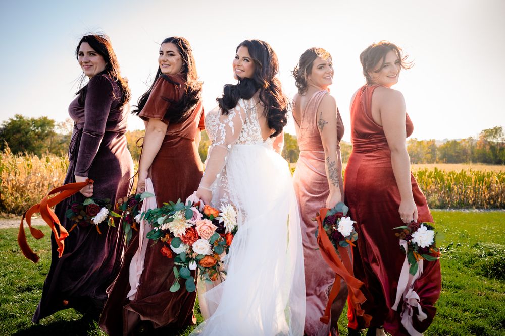 Bridal party in burgundy dresses walking together across sunny outdoor venue.